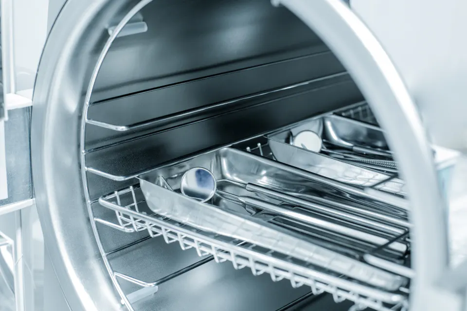 Stainless steel instrument trays loaded inside an open steriliser.